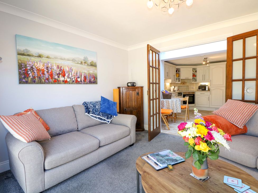 A living room with two sofas a wooden coffee table with flowers and an open door to a kitchen at Lavender Cottage in Hailsham