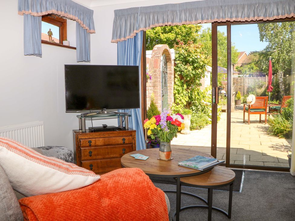 A living room with a television on a wooden chest and a coffee table with flowers and a book at Lavender Cottage in Hailsham