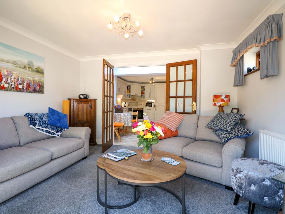 A living room with two sofas a round wooden coffee table and open double doors leading to a kitchen at Lavender Cottage in Hailsham