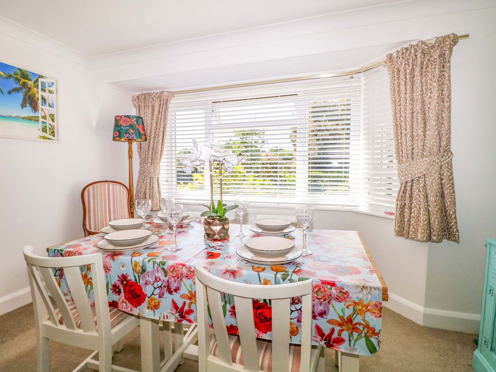 A dining room with a floral tablecloth on the table set with plates and glasses and windows with blinds and curtains at Lavender Cottage in Hailsham