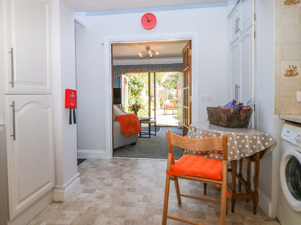 A kitchen with a small table and wooden chair with orange cushion next to a washing machine at Lavender Cottage in Hailsham