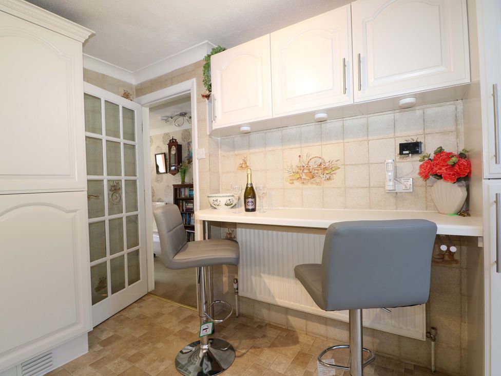 A kitchen area with two bar stools a countertop and white cabinets at Lavender Cottage in Hailsham