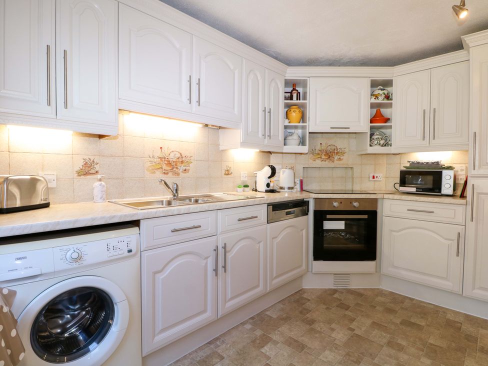 A kitchen with white cabinets a washing machine a toaster a microwave and an oven at Lavender Cottage in Hailsham