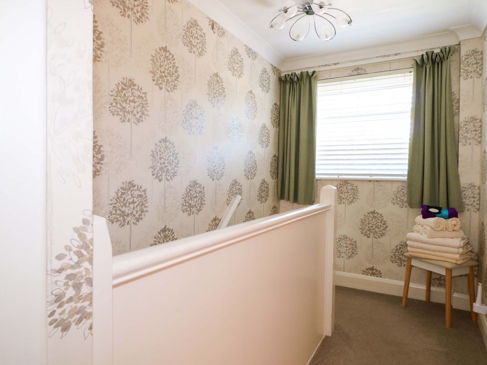A hallway with floral wallpaper a window with green curtains and a stool with folded towels at Lavender Cottage in Hailsham