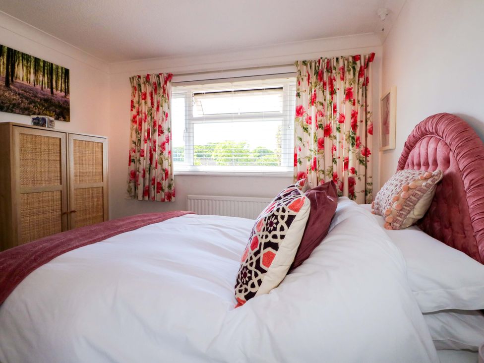 A bedroom with a bed with cushions and floral curtains on the window at Lavender Cottage in Hailsham