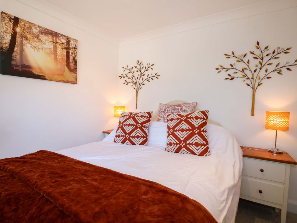 A bedroom with a bed white bedding and orange pillows and blanket beside nightstands with lamps at Lavender Cottage in Hailsham