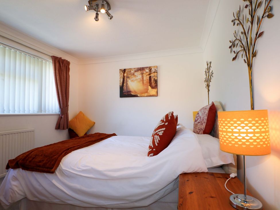 A bedroom with a bed pillows a side table and a lamp at Lavender Cottage in Hailsham