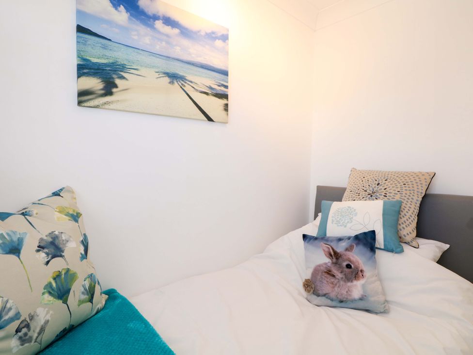 A small bedroom with a bed that has three decorative pillows and a beach scene photo on the wall at Lavender Cottage in Hailsham