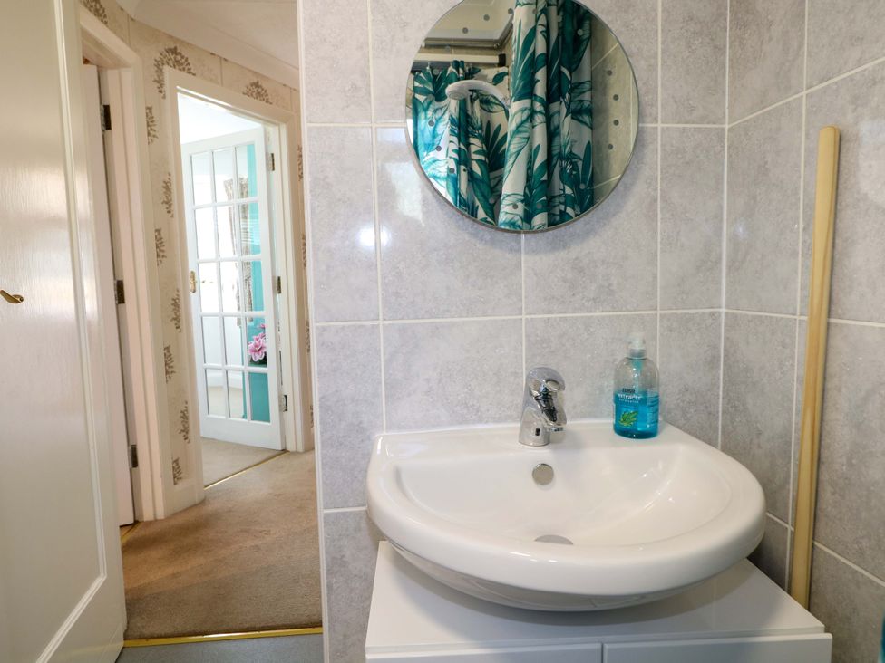 A bathroom sink with a round mirror above and a bottle of hand soap on the sink at Lavender Cottage in Hailsham