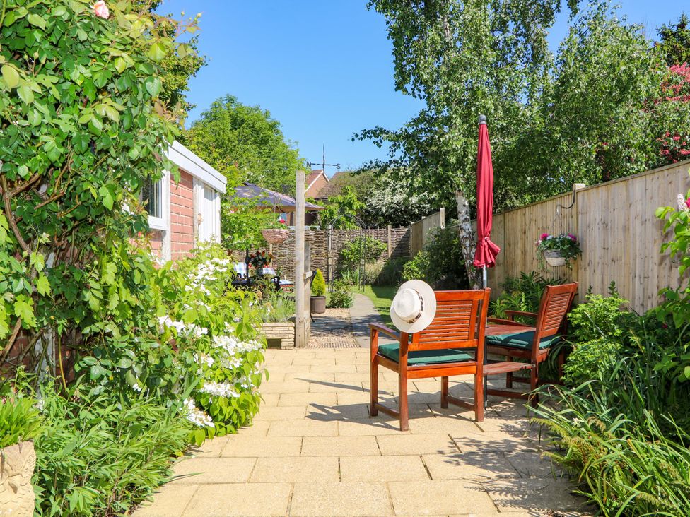 A garden patio with wooden chairs a red umbrella and various plants at Lavender Cottage in Hailsham