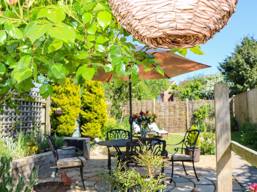 A garden patio with a table and chairs under an umbrella and greenery at Lavender Cottage in Hailsham