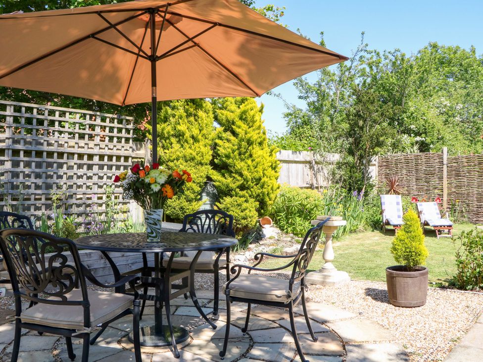 A garden patio with a round table and umbrella surrounded by four chairs and flowers in a vase at Lavender Cottage in Hailsham