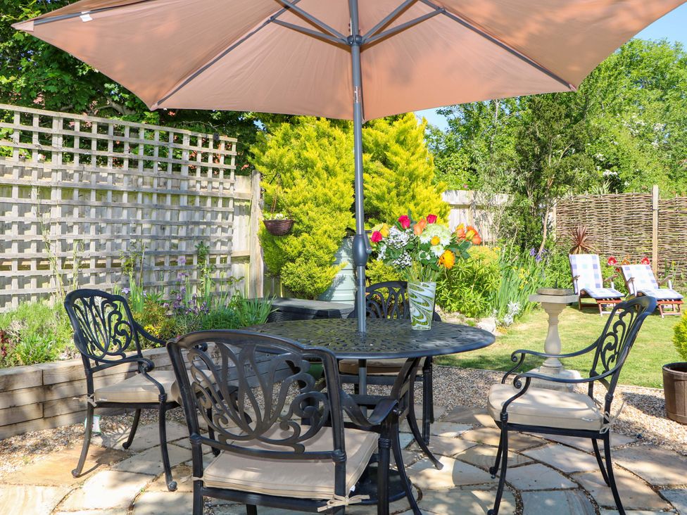 An outdoor patio with a metal table and chairs under a large umbrella with flowers on the table and garden in the background at Lavender Cottage Hailsham