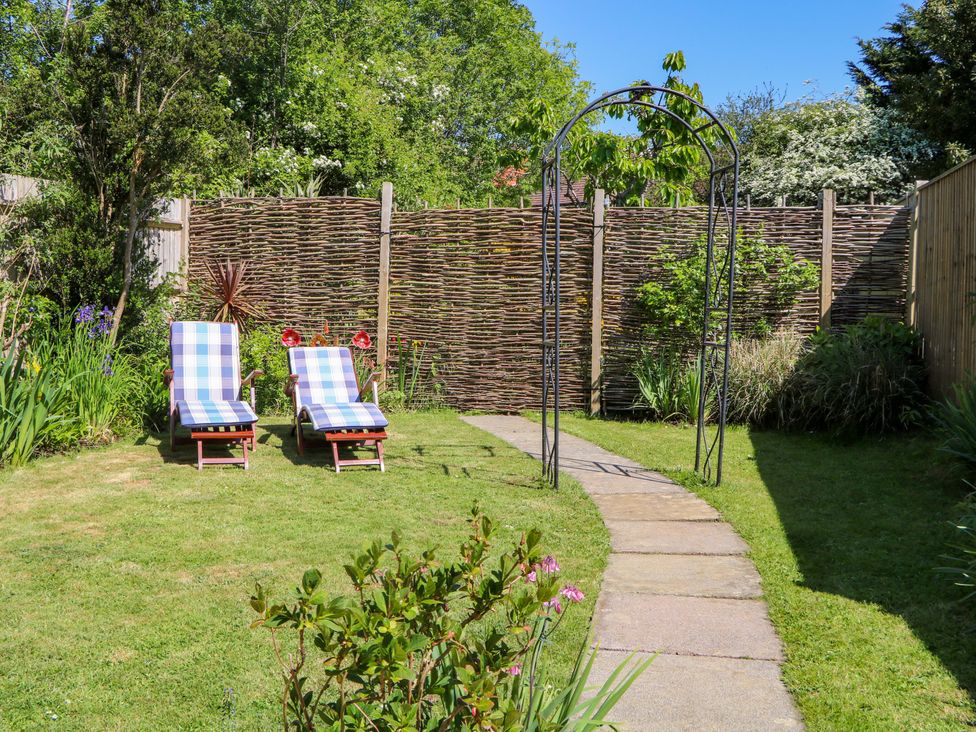 A garden with two lounge chairs on grass and a stone path with an arch at Lavender Cottage in Hailsham