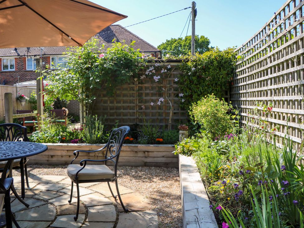 A garden patio with a round metal table and chairs under an umbrella and a wooden fence with climbing plants at Lavender Cottage in Hailsham