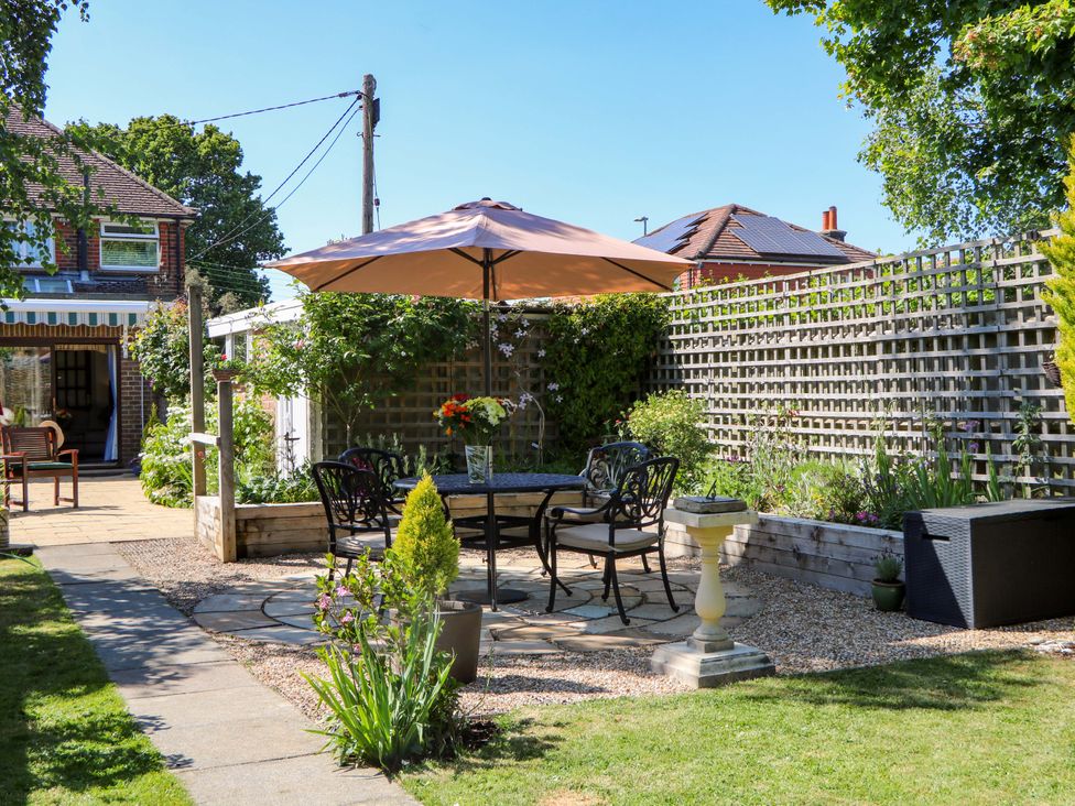A garden patio with a table and chairs under an umbrella surrounded by plants and a house in the background at Lavender Cottage in Hailsham