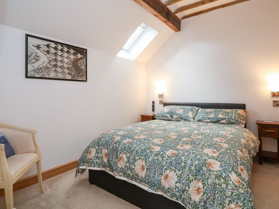 A bedroom with a bed, bedside tables, a chair, and artwork at The Stables in Chester