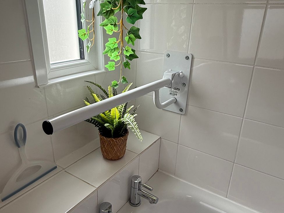 A bathroom with a grab bar and a plant at Waves End in Mevagissey