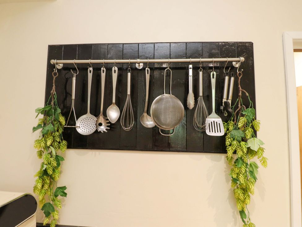 A kitchen wall with hanging cooking utensils and greenery at Mallards Rest Llandwrog near Bontnewydd Gwynedd