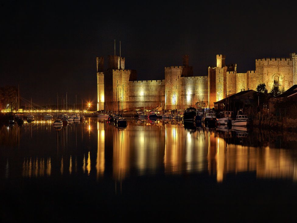 A castle by the water with boats at night at Mallards Rest in Llandwrog near Bontnewydd, Gwynedd