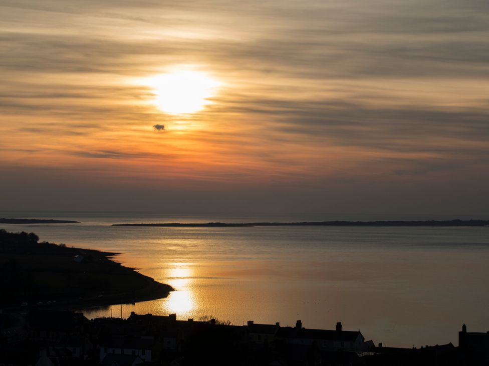 A sunset over a body of water with buildings in the foreground at Mallards Rest, Llandwrog near Bontnewydd, Gwynedd