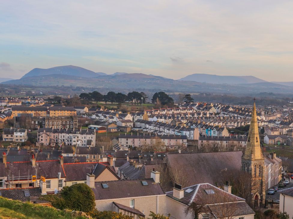 A view of houses and a church with mountains in the background at Mallards Rest in Llandwrog near Bontnewydd, Gwynedd