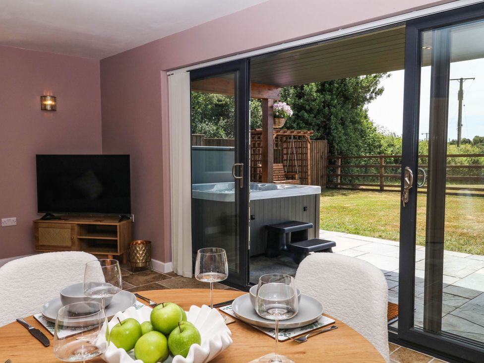 A dining room with a table set for meals and a hot tub visible through sliding glass doors at Harescombe Lodge Morchard Bishop