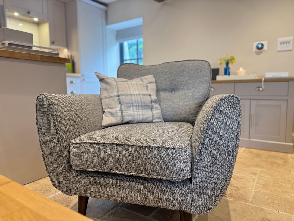 A living room with an armchair and kitchenette at Railway Cottage in Penybontfawr