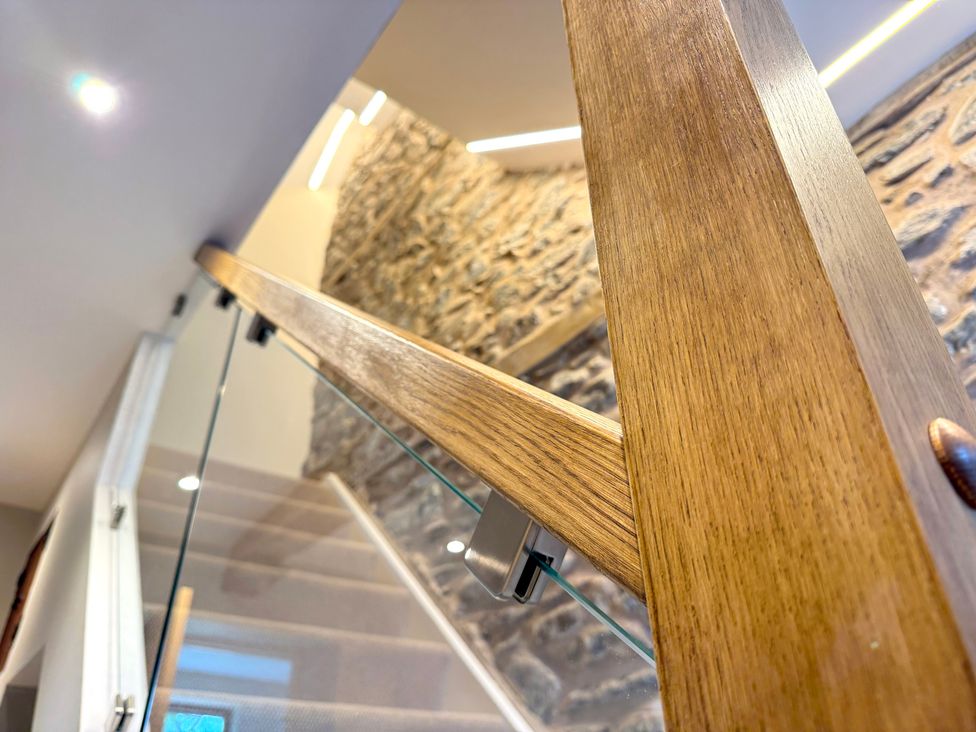 A staircase with wooden handrail and glass balustrade at Railway Cottage Penybontfawr