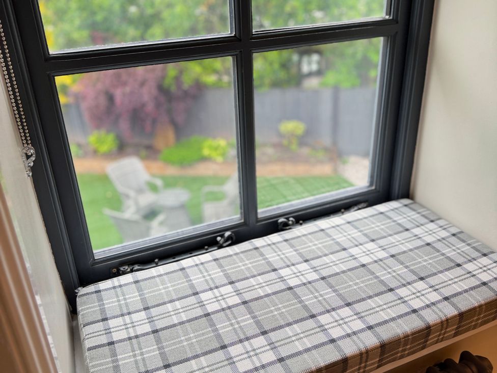 A window seat with a plaid cushion overlooking a garden at Railway Cottage Penybontfawr