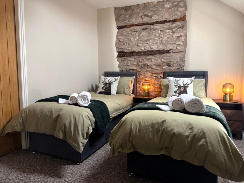 A bedroom with two beds and a stone wall at Railway Cottage in Penybontfawr