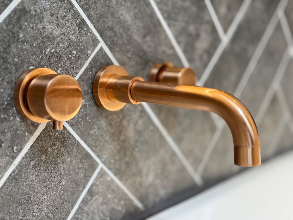 A copper faucet with handles on a tiled wall at Railway Cottage in Penybontfawr