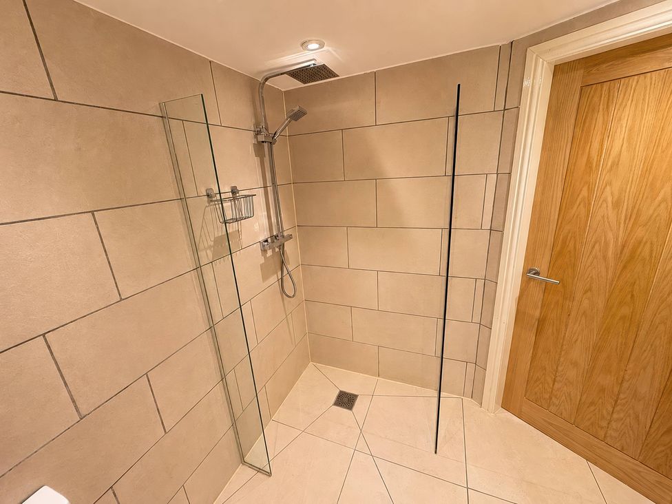 A shower with glass screen and tiled wall at Railway Cottage in Penybontfawr