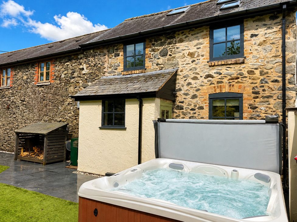 An outdoor area with a hot tub and a stone house at Railway Cottage in Penybontfawr