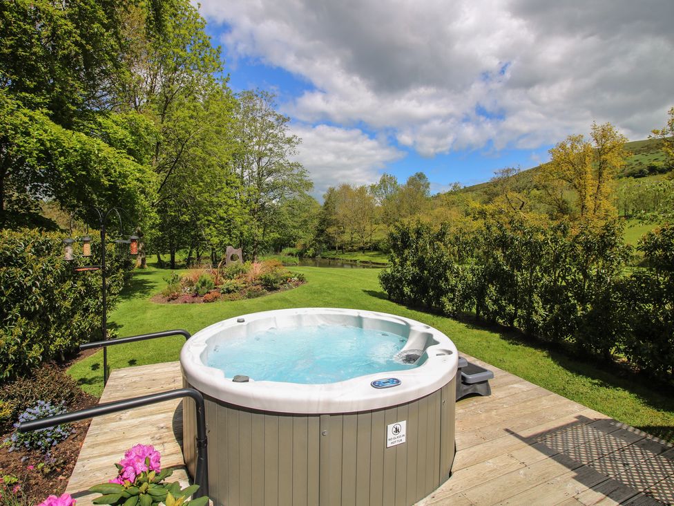 A hot tub on a deck surrounded by greenery at Pultheley Cottage Hyssington near Churchstoke