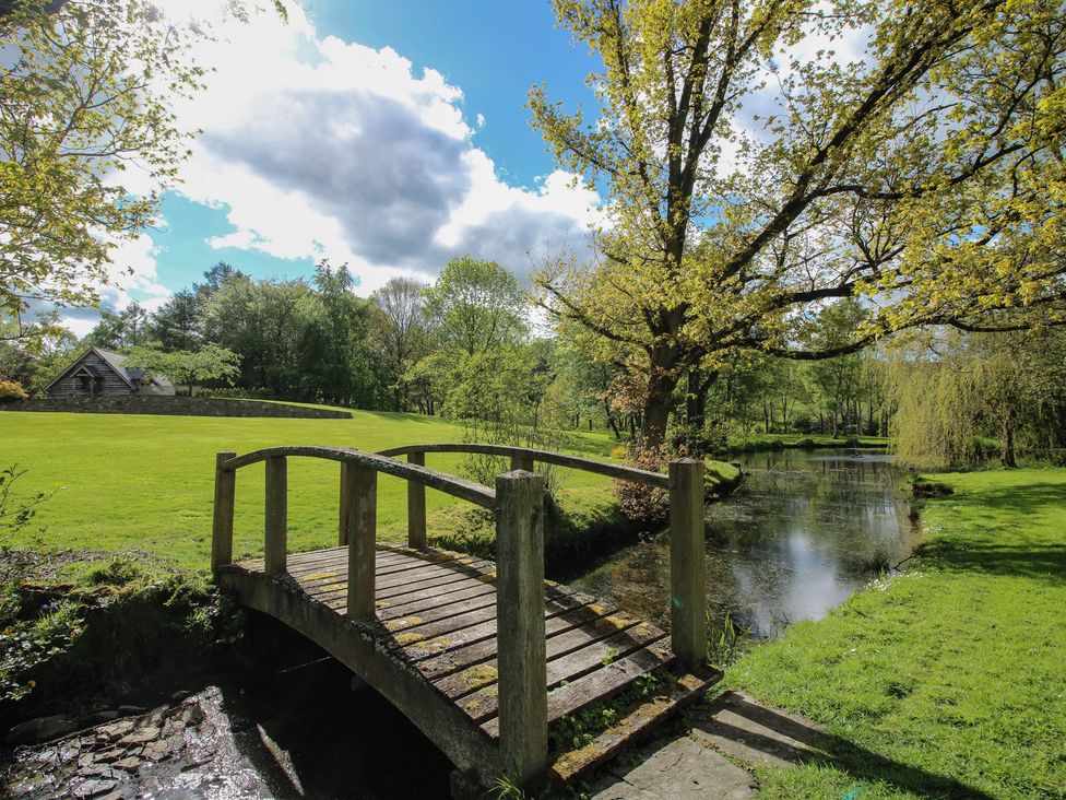 An outdoor area with a bridge over a pond and a cottage in the background at Pultheley Cottage near Hyssington