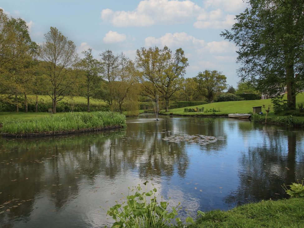 A serene pond with trees and grass at Pultheley Cottage Hyssington near Churchstoke