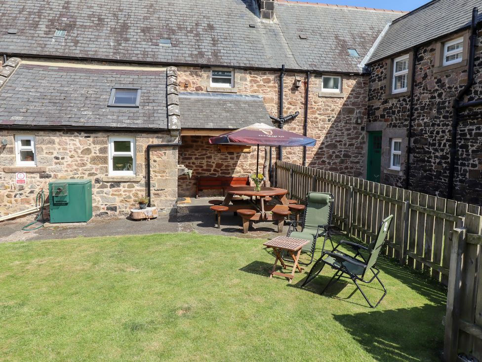 A garden with a wooden table and chairs at Kits Cottage Middleton near Belford