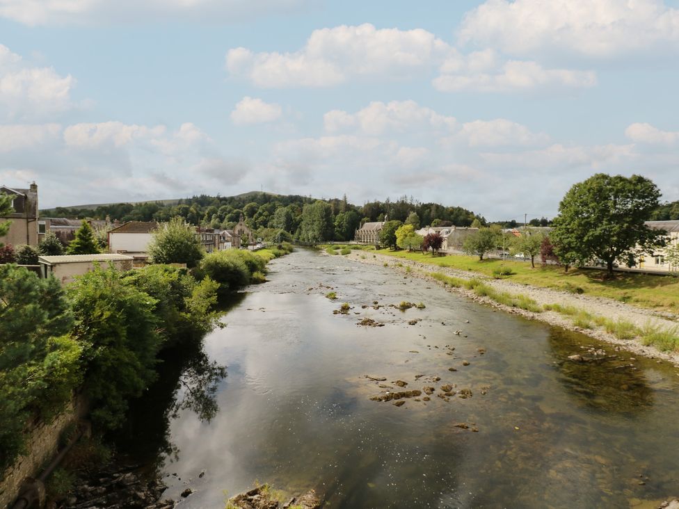 A river with buildings and trees in the background at Eskvale House in Langholm