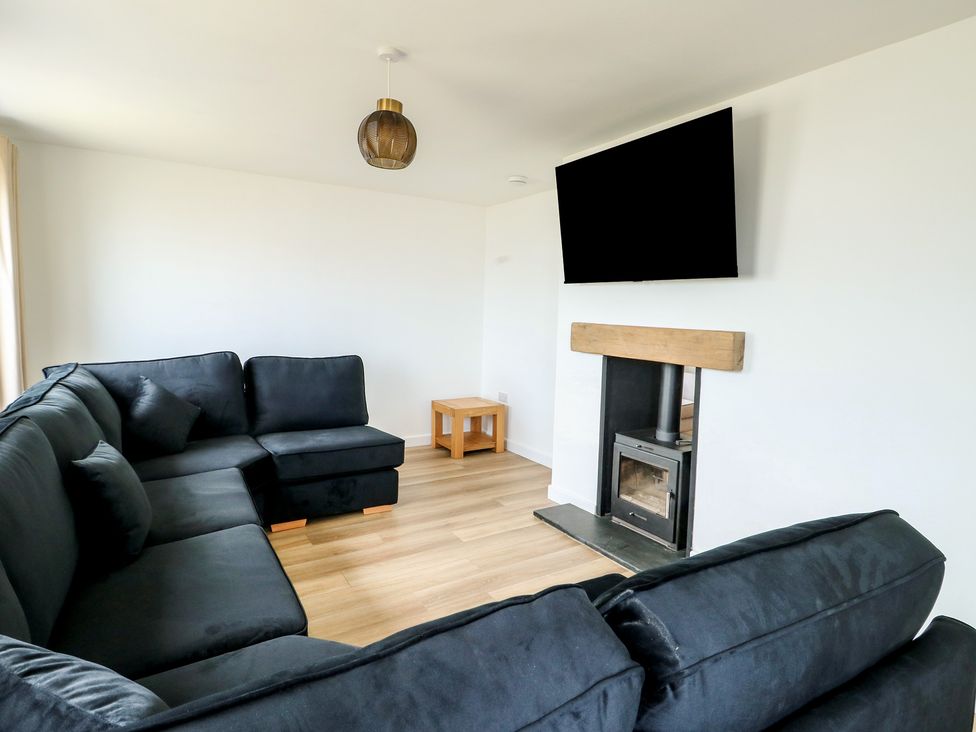 A living room with a sofa, coffee table, fireplace, and television at 6 Gwelfor Estate