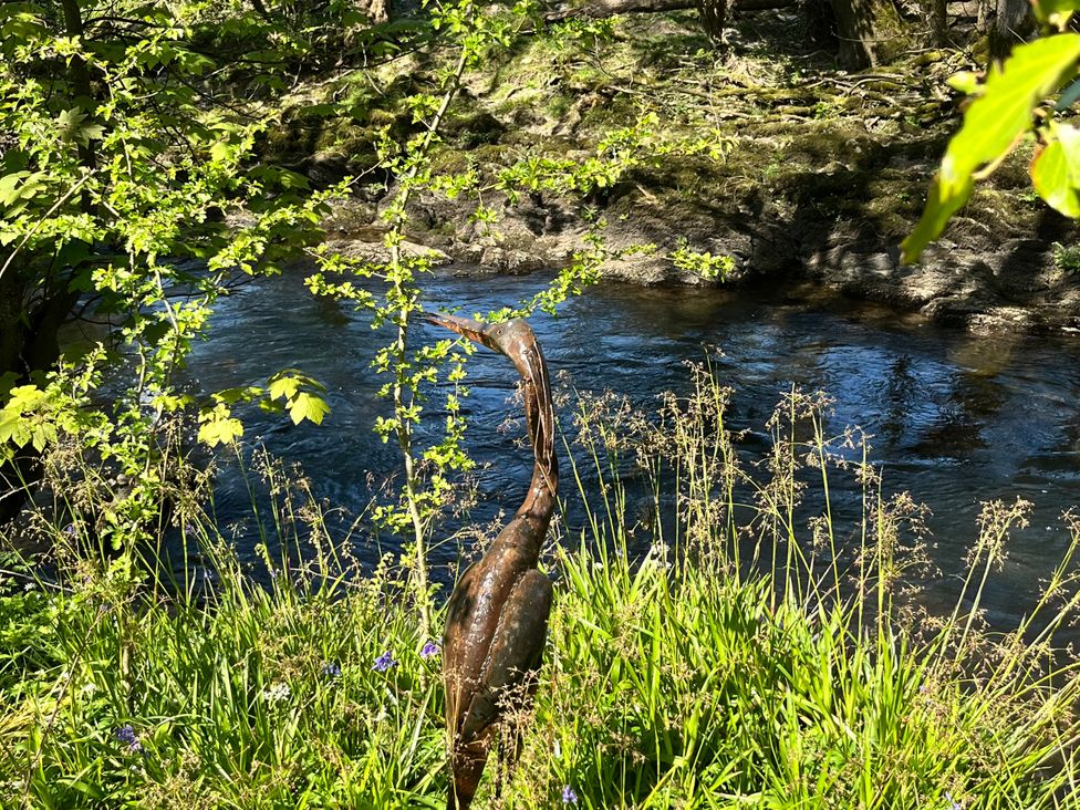 A heron sculpture near a river with grass and flowers at Glas y Dorlan near Newport, Pembrokeshire