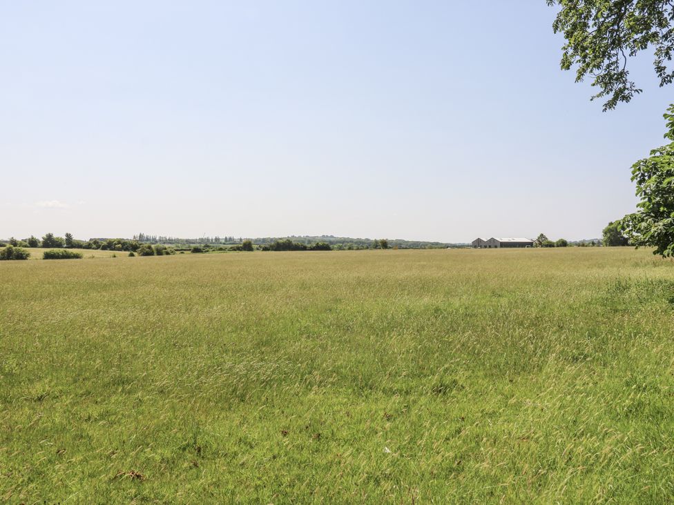 A grassy field with trees and a building at Little Yeat Farm in Aylesbury