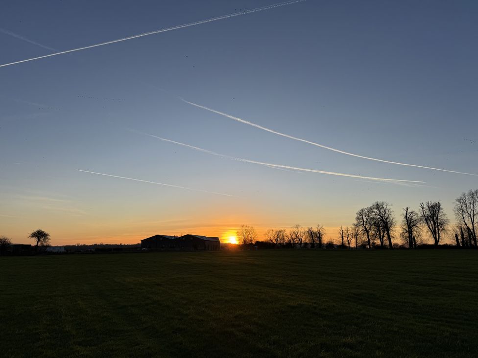 A sunset behind trees and a building in a field at Number 2 The Barn House Woodham