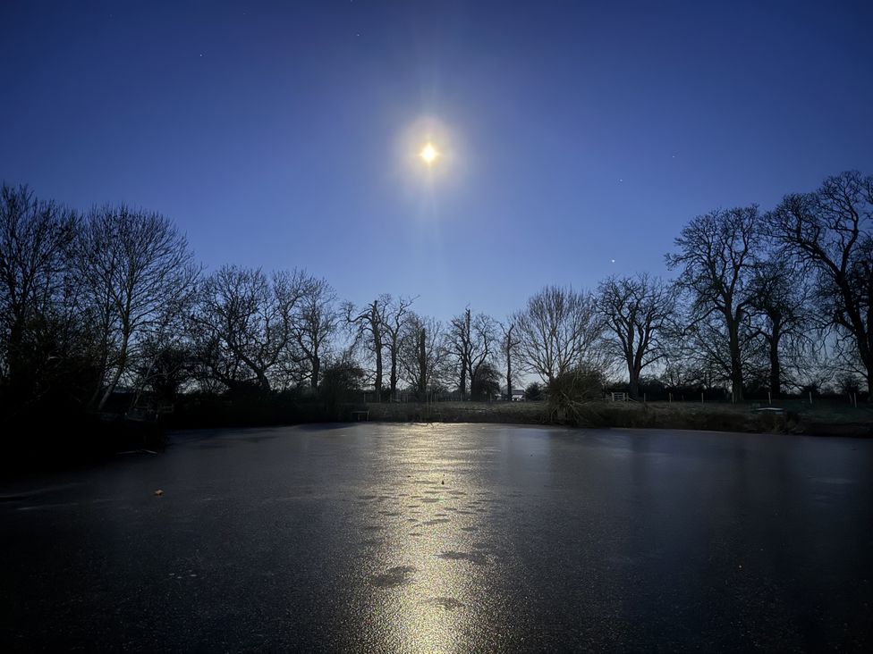 A frozen pond with moonlight reflection and trees at Number 2 The Barn House in Woodham