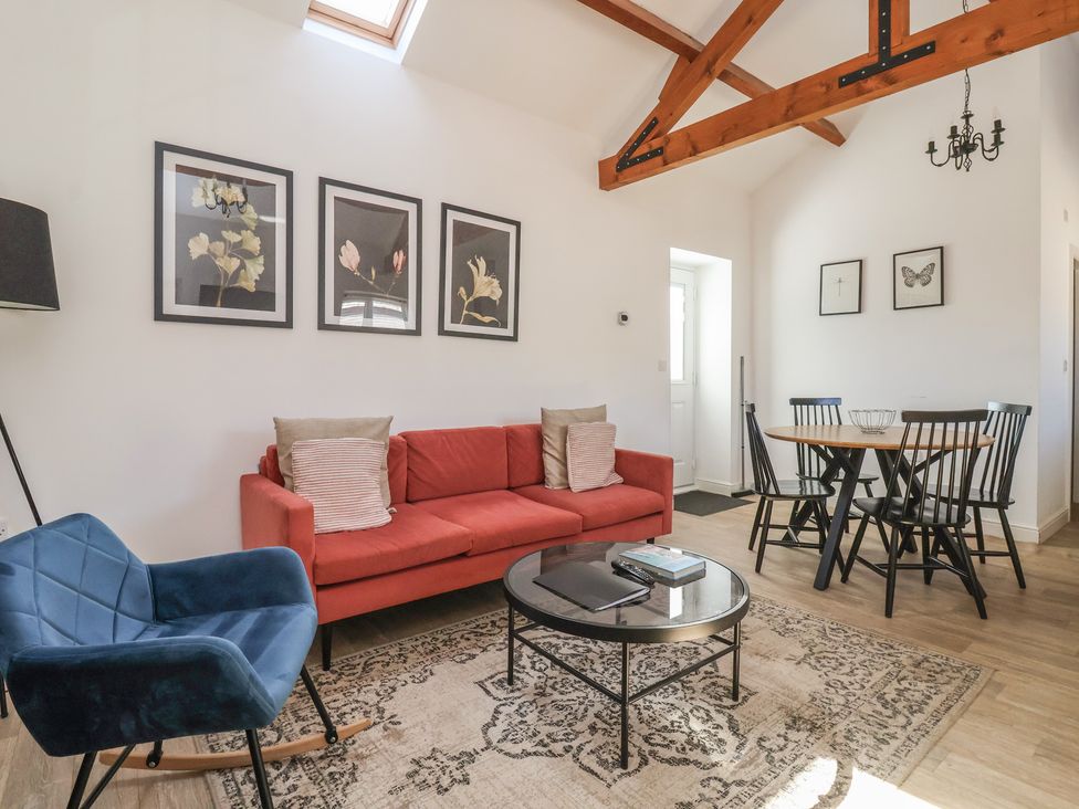 A living room with a red sofa blue rocking chair round glass coffee table and dining table with black chairs at Guillemot in Flamborough