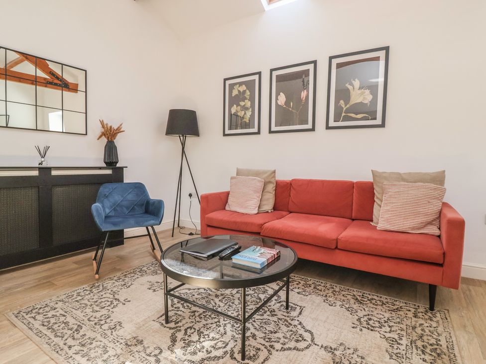 A living room with a red sofa a blue chair a round glass coffee table a standing lamp and framed flower pictures on the wall at Guillemot in Flamborough