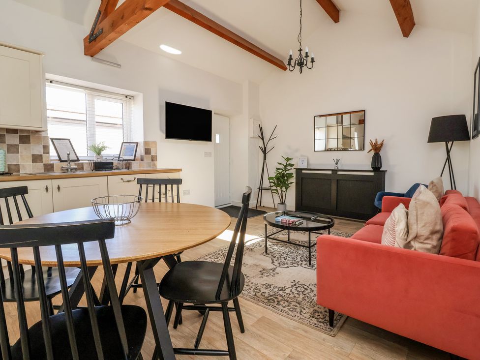 A living room and kitchen area with a round wooden table and black chairs a red sofa and a black cabinet with a mirror above it at Guillemot in Flamborough