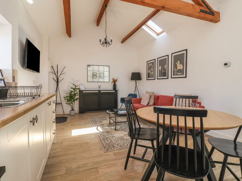 A kitchen and living room area with a round wooden dining table and black chairs a red sofa a black cabinet and wooden ceiling beams at Guillemot in Flamborough