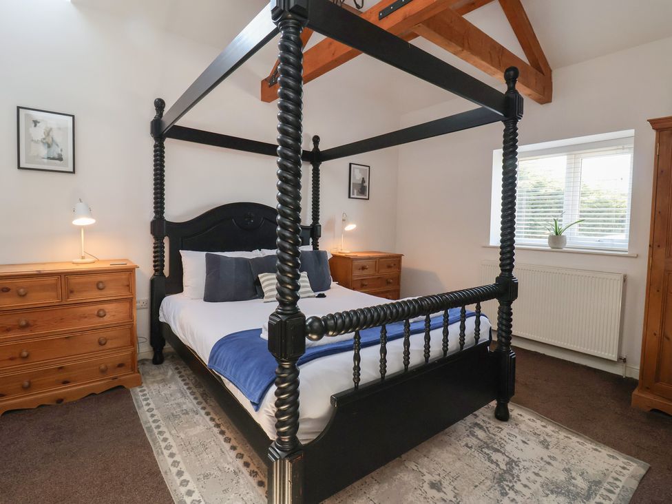 A bedroom with a black four-poster bed two wooden dressers lamps a window and a rug at Guillemot in Flamborough