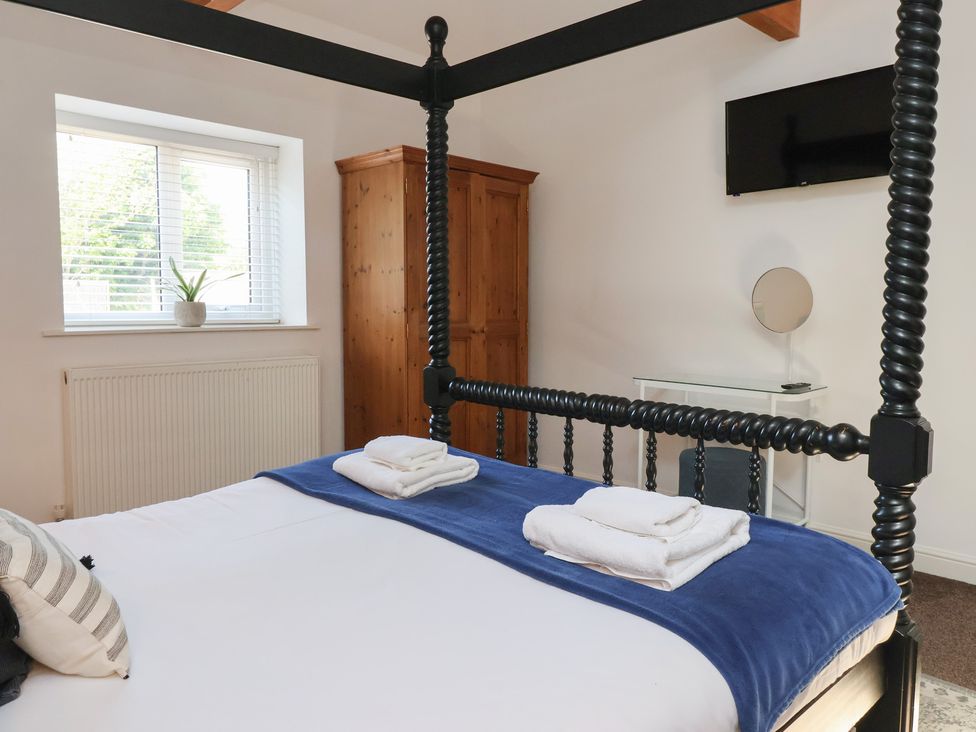 A bedroom with a four poster bed folded towels on the bed a wooden wardrobe a window with blinds and a wall mounted television at Guillemot in Flamborough